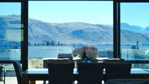 A dining area with a table and chairs, a vase with flowers, and a view of mountains through large windows.