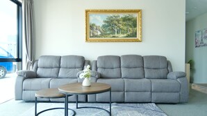 A living room with a grey sofa, a round wooden coffee table, and a framed painting on the wall. - Stargazing Tekapo Apartment C (Lake Tekapo)