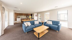 Una sala de estar moderna con un sofá azul, una mesa de centro de madera y una cocina al fondo.