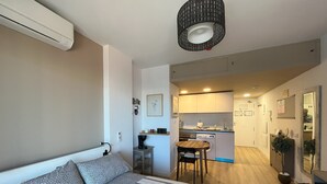 A compact bedroom with a bed, bedside table, and a small kitchenette in the background.