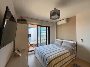 Un dormitorio con cama, televisión, lámpara en el techo y puerta corrediza a un balcón.
