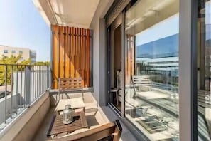A balcony with a wooden table, a chair, and a view of a building through glass doors.