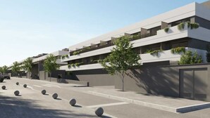 A modern multi-story building with balconies, a parking area with bollards, and a clear sky.