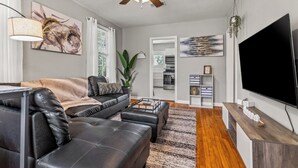 Un salon moderne avec un canapé en cuir noir, une table basse, un téléviseur à écran plat et un ventilateur de plafond.