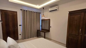 Habitació d'hotel amb un llit gran, un ventilador de sostre, un aparell d'aire condicionat i portes de fusta.