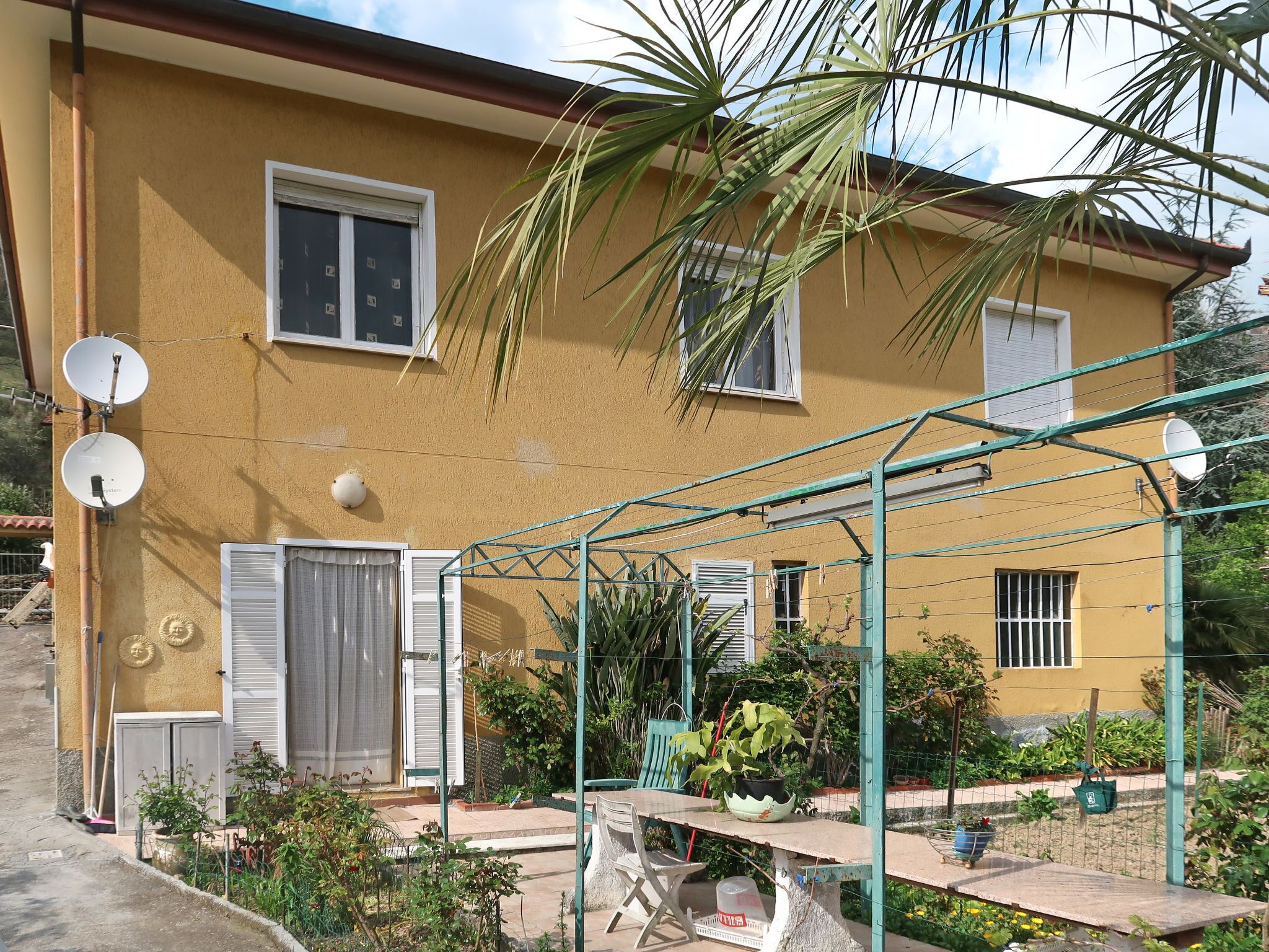 A yellow building with satellite dishes, a covered patio, and potted plants.