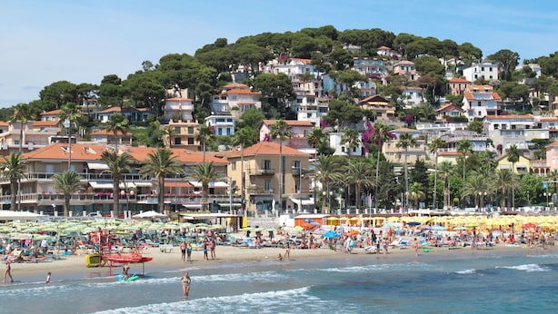 A coastal town with a beach, buildings, and palm trees.