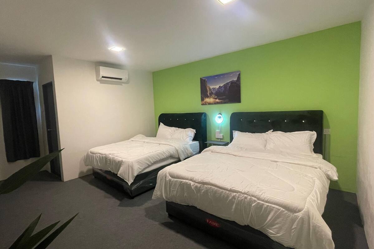 A hotel room with two beds, a green accent wall, a painting, and a ceiling light.