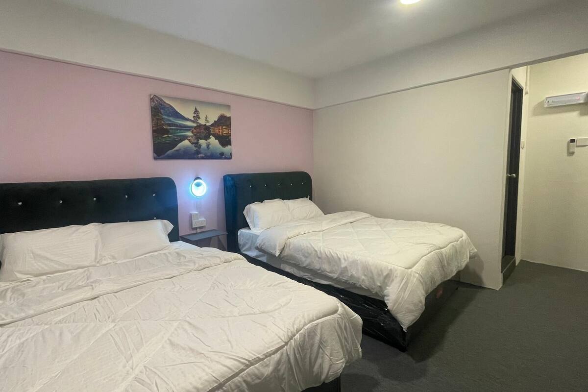 A hotel room with two single beds, a nightstand with a lamp, a painting on the wall, and a door to the right.