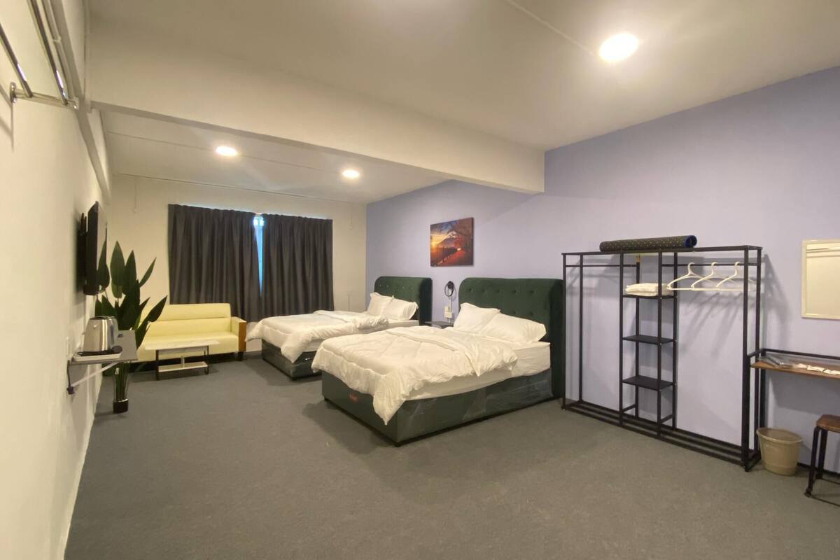 A hotel room with two beds, a desk, a chair, a plant, and a window with curtains.