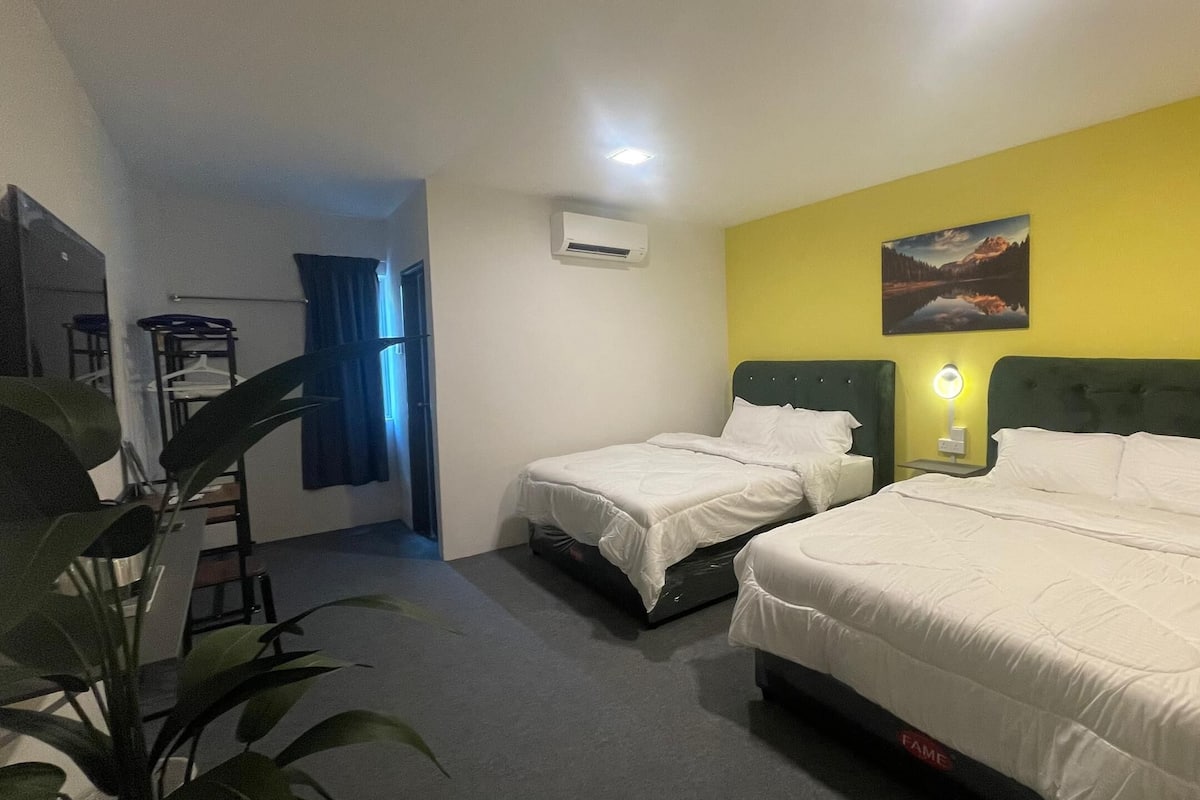 A hotel room with two single beds, a desk, a chair, an air conditioning unit, and a painting on the wall.