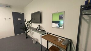 A small, compact room with a desk, a chair, a bed, and a mirror. - RAZO VILLAGE INN (Taiping)