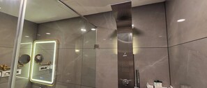 Ein modernes Badezimmer mit Duschabtrennung aus Glas, einem Spiegel mit goldener Rahmung und einer Wand mit dem Jaguar-Logo.