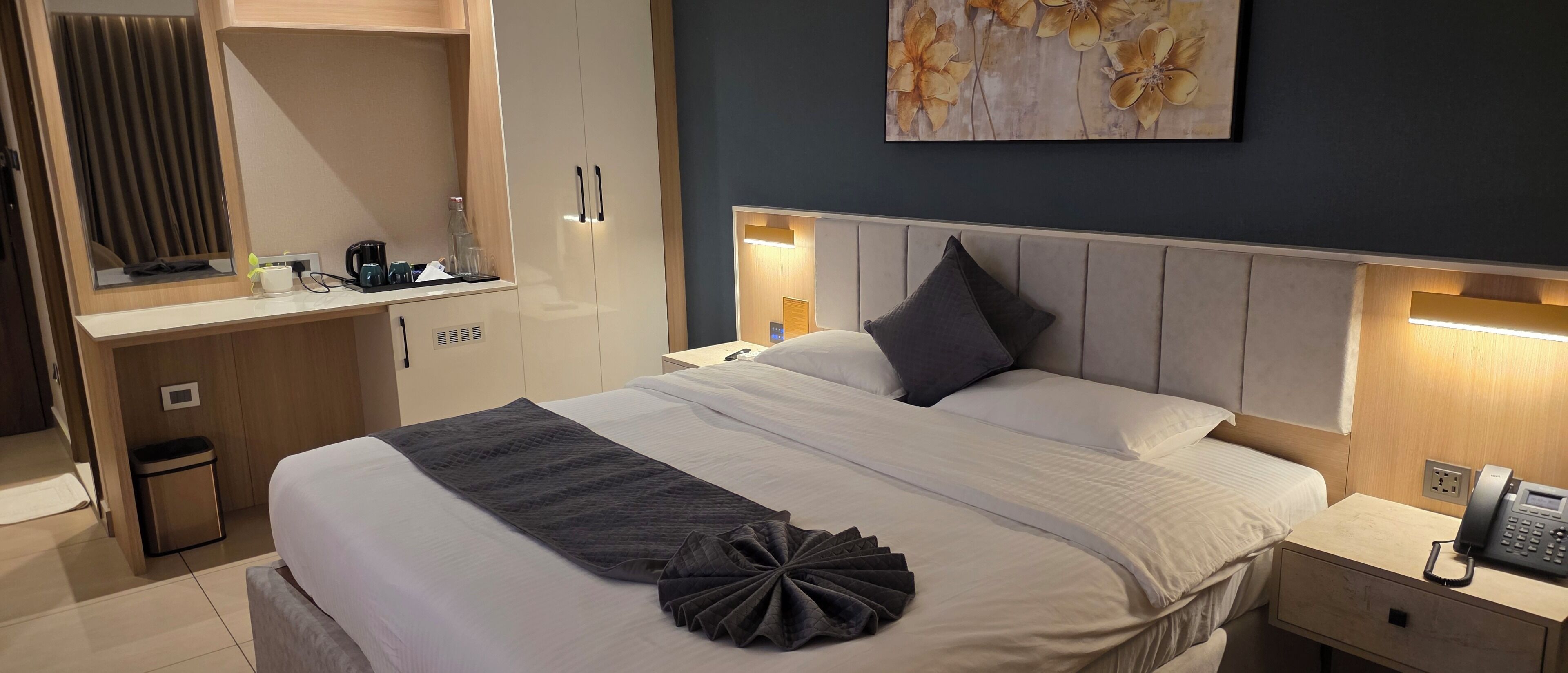 A neatly made bed with a decorative pillow, a bedside table with a phone, and a wall-mounted artwork.