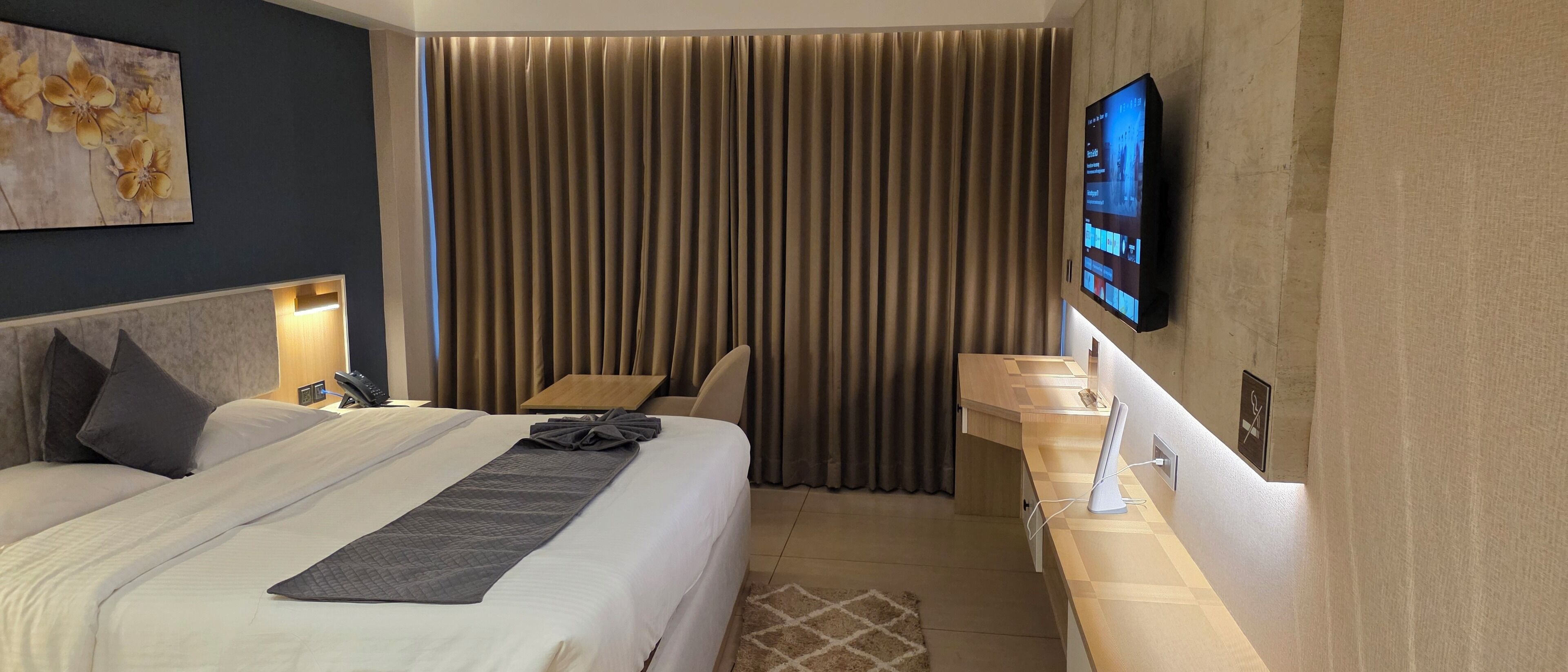 A hotel room with a bed, bedside table, TV, and curtains.