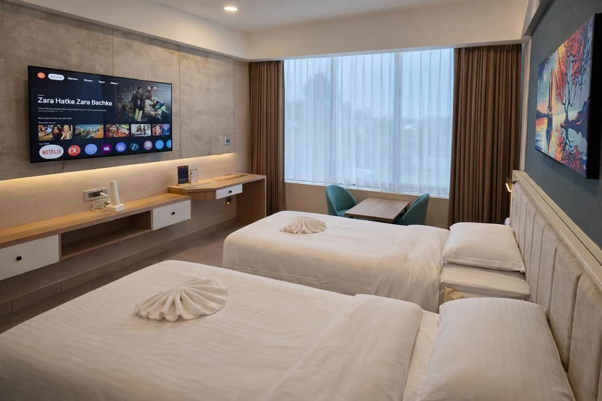 Een hotelkamer met twee bedden, een bureau, een aan de muur bevestigde televisie en een raam met gordijnen.