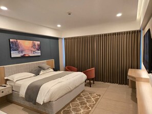 Ein modernes Hotelzimmer mit einem großen Bett, einem Nachttisch, einem Sessel, einem Fernseher und einem Bild an der Wand.