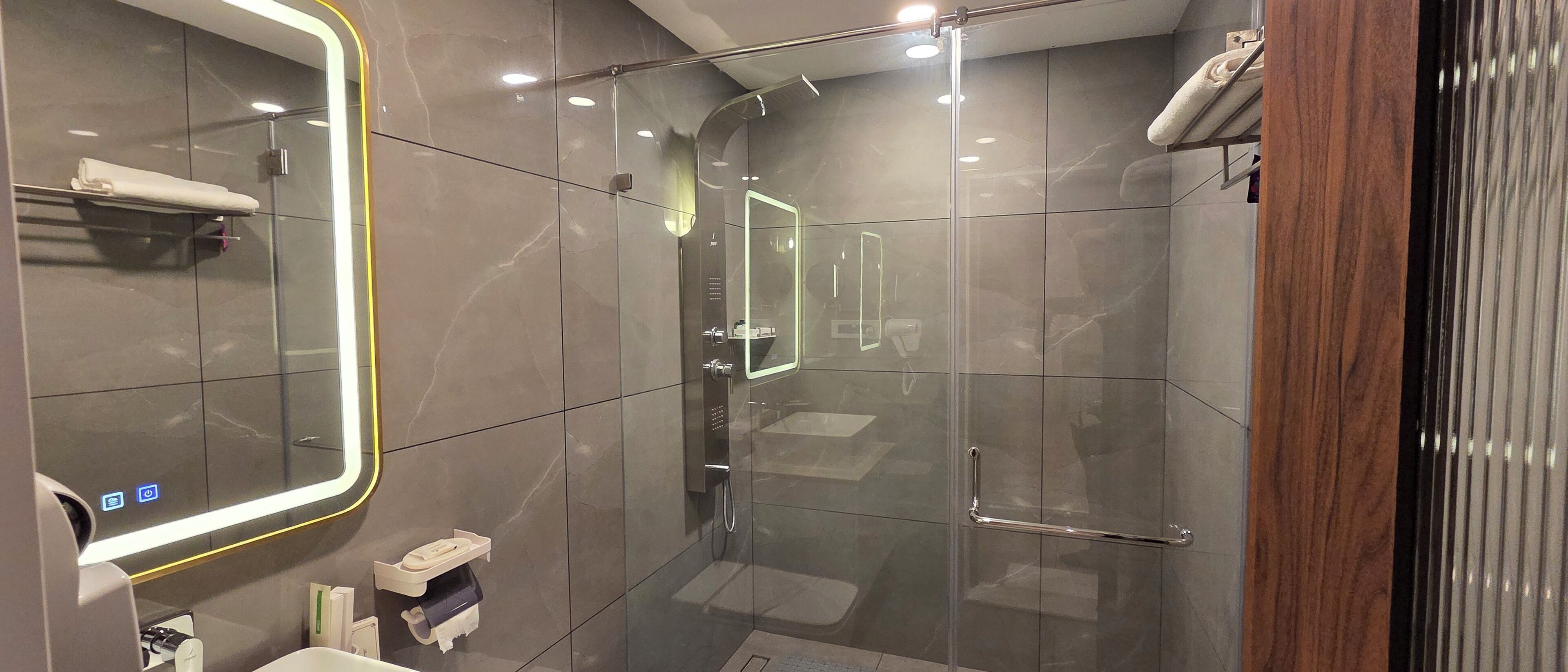 Ein modernes Badezimmer mit Duschkabine aus Glas, einem großen Spiegel und einem Handtuchhalter.