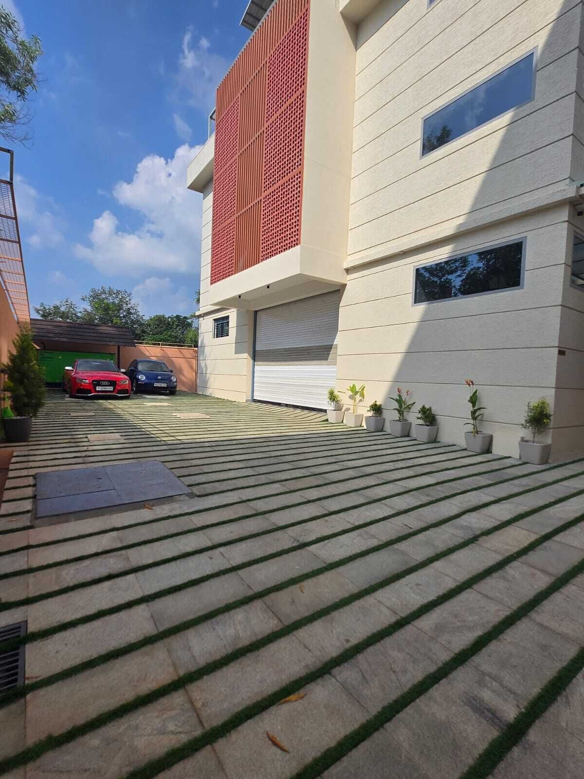 A modern building with a red facade, a covered garage, and a paved driveway with potted plants.