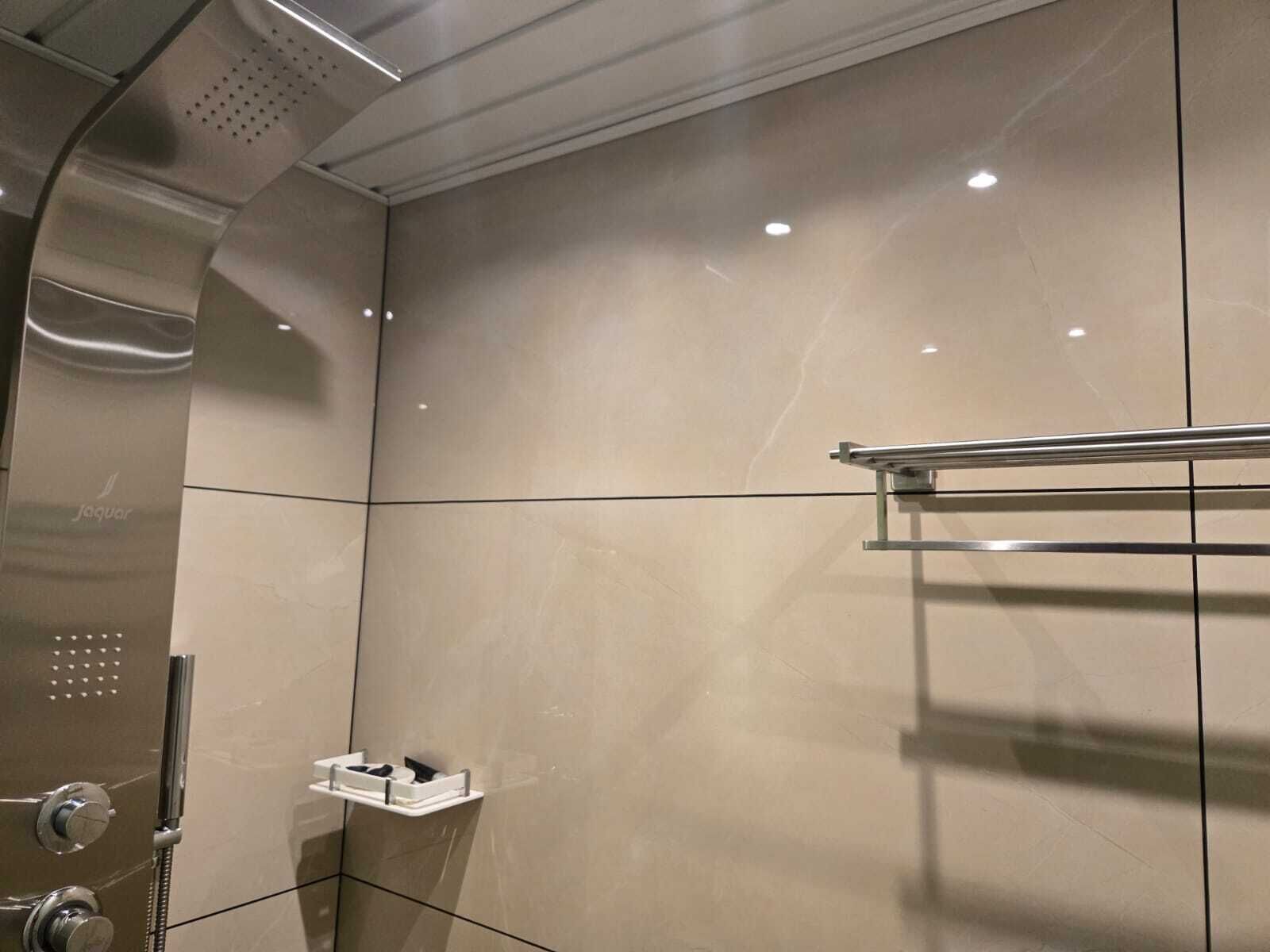 Et moderne badeværelse med et glasafskærmet brusebad, et håndklædetørrestativ og en lille hylde med toiletartikler.