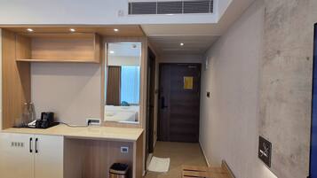 Habitación de hotel con minibar, espejo, mueble de madera, cubo de basura y una pantalla digital mostrando contenido.