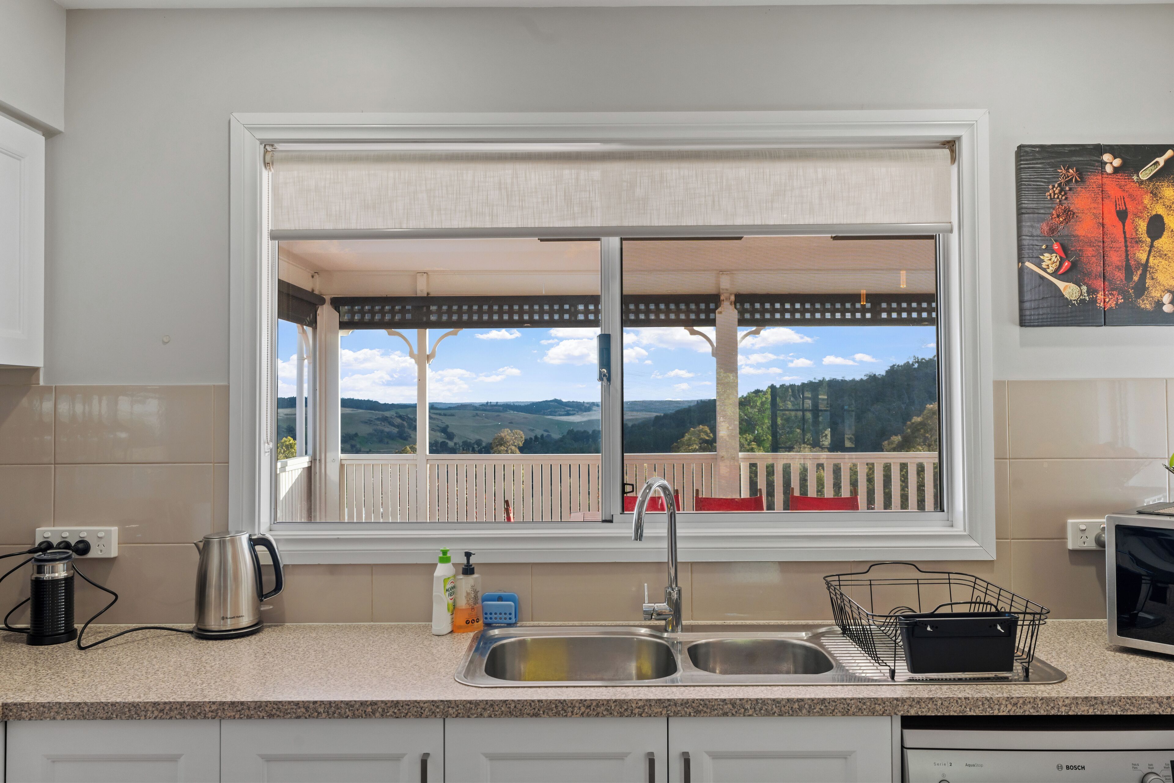 A kitchen with a large window, a sink, a kettle, and a Bosch dishwasher.