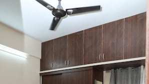 Un dormitorio con cama, armario de madera oscura, ventilador de techo y cortinas grises.