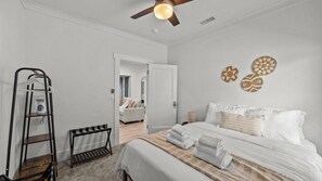 Ein Schlafzimmer mit einem Bett, einer Holzleiter, einem Deckenventilator und einer Tür zu einem anderen Raum.