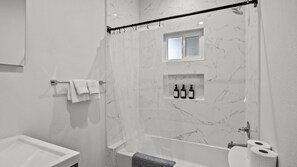 Ein modernes Badezimmer mit Dusche, Toilette und Waschbecken. Handtücher hängen an einem Handtuchhalter und ein Regal mit Pflegeprodukten ist vorhanden.