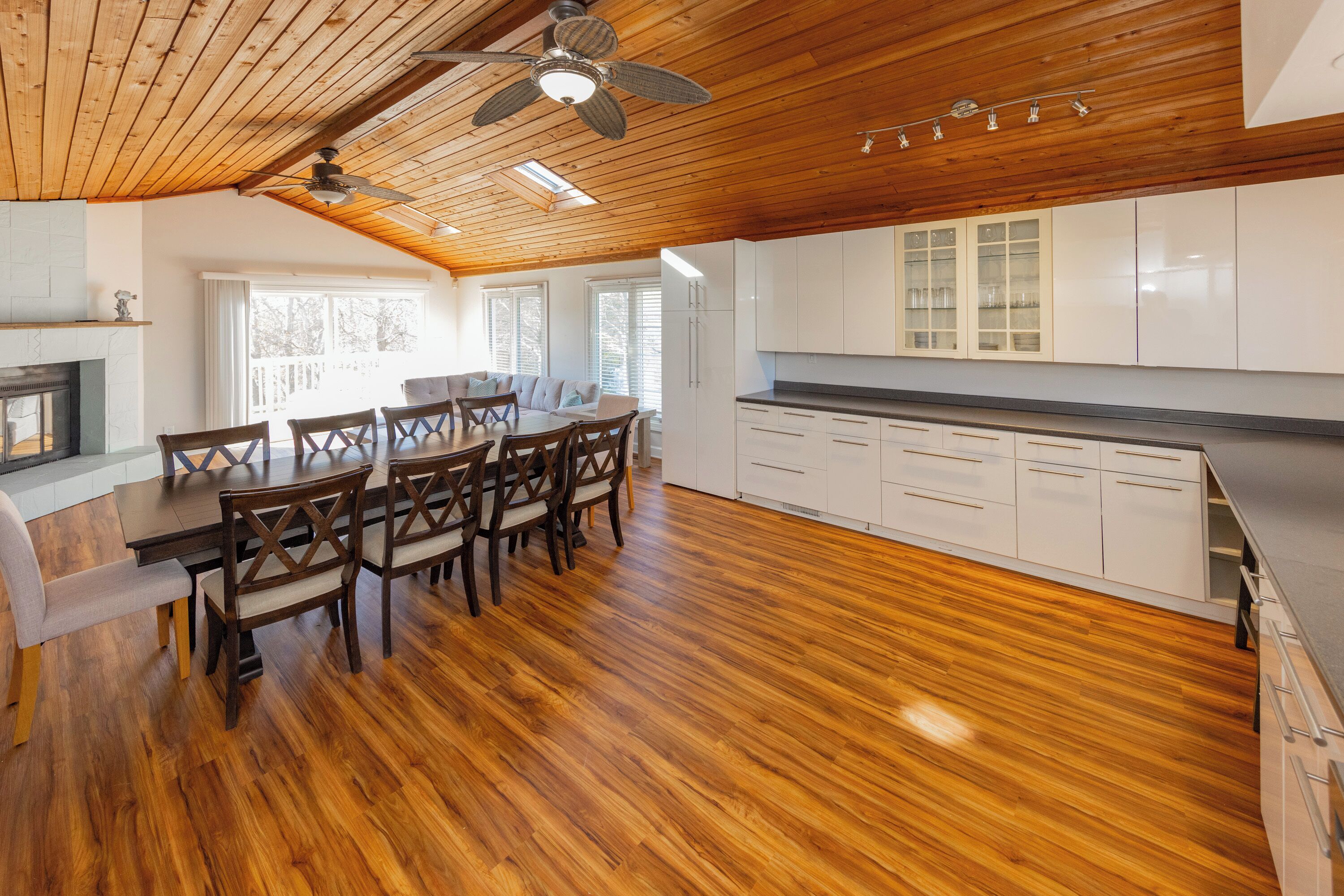 Une cuisine spacieuse dotée d’un plancher en bois, de meubles blancs et d’un coin repas avec des chaises et une table en bois.