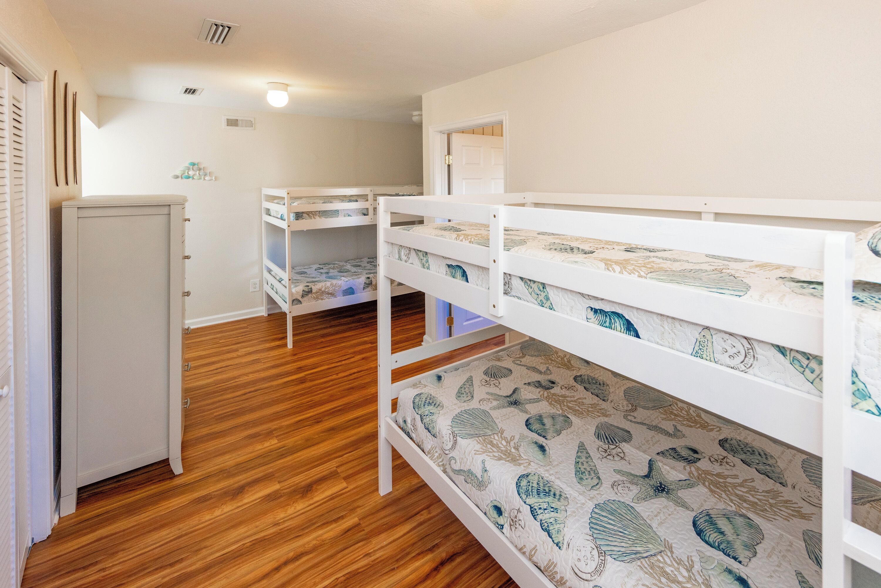 Un dormitorio con literas, suelo de madera, un armario blanco y una puerta que da a otra habitación.