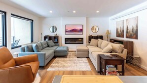 A modern living room with a sectional sofa, a loveseat, and a chair. There is a fireplace, artwork on the walls, and a large window providing natural light.