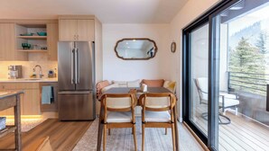 A modern kitchen with a stainless steel refrigerator, wooden cabinets, and a dining area with two wicker chairs and a table.
