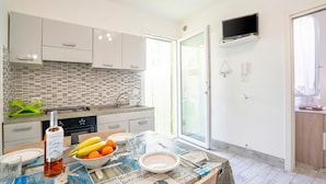 A modern kitchen with white cabinets, a tiled backsplash, a dining table set with plates, a bottle, and fruit. - Casa Graziano 1 Near Sandy Beach, Porto Cesareo, Italy (Porto Cesareo)