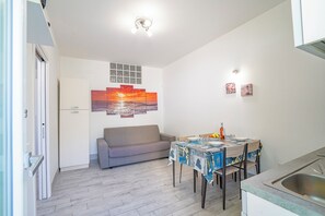 A compact living space with a kitchenette, a dining table with chairs, a sofa, and wall art. - Casa Graziano 1 Near Sandy Beach, Porto Cesareo, Italy (Porto Cesareo)