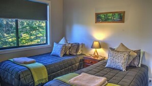 Quarto com duas camas, janela com vista para o verde, um quadro na parede e uma luminária de cabeceira.