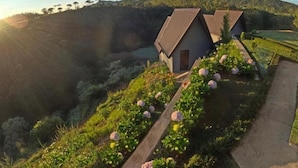 Una propiedad en una ladera con dos casas pequeñas, un jardín de flores rosas y vistas a un valle.