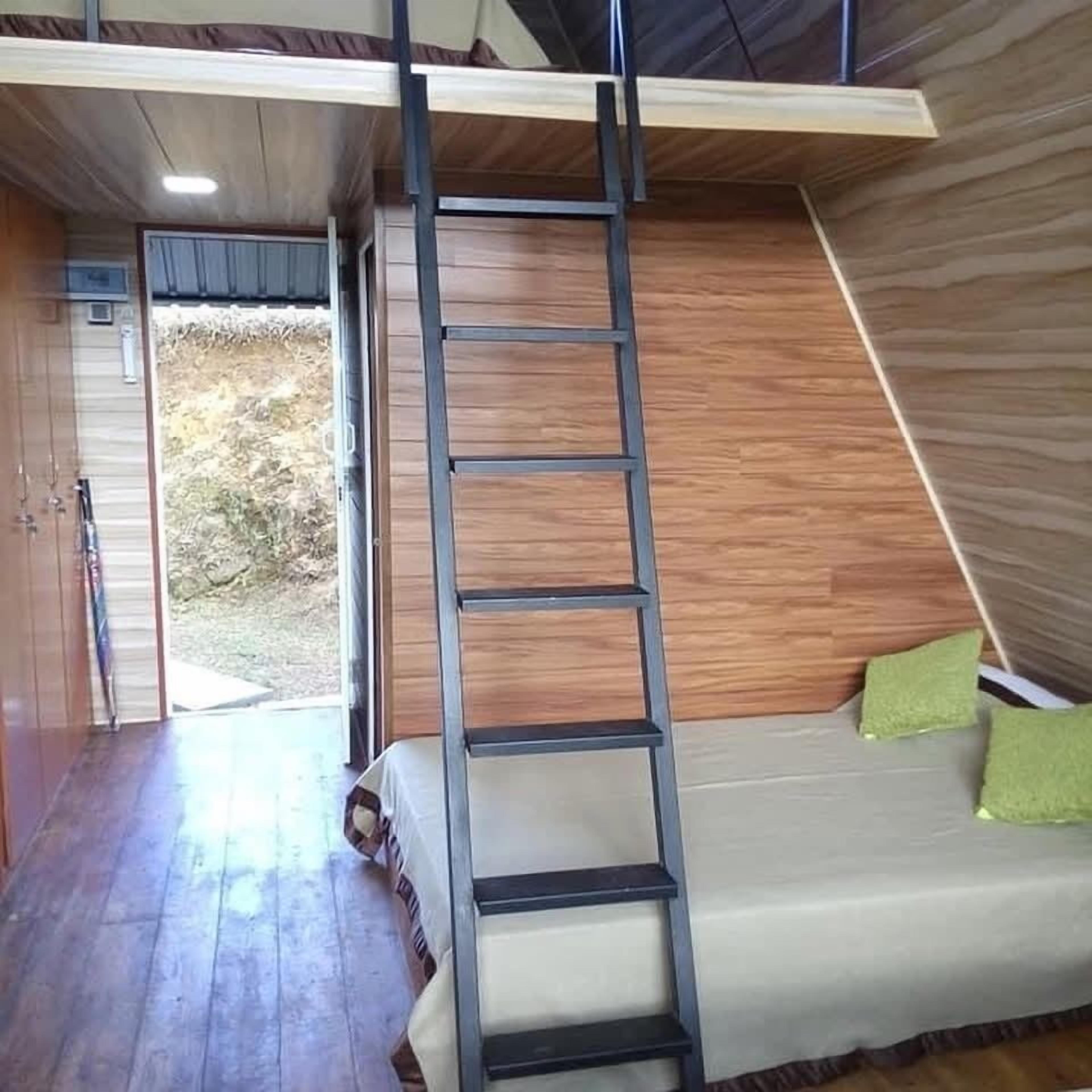 A room with a wooden floor, a sofa with green cushions, and a ladder against the wall.