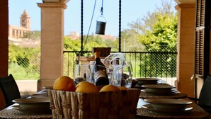 Une table à manger est dressée avec des assiettes, des verres et une bouteille, et un panier d’oranges est placé au premier plan.
