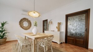 Un coin repas comprenant une table en bois, des chaises blanches, un luminaire suspendu et un élément décoratif mural.