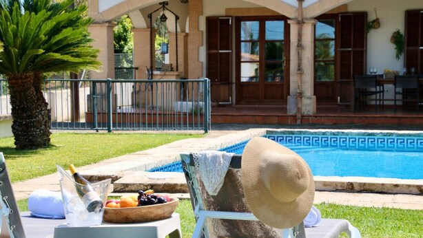 Un espace aménagé au bord de la piscine, avec un fauteuil de relaxation, une bouteille de champagne et un saladier rempli de fruits.