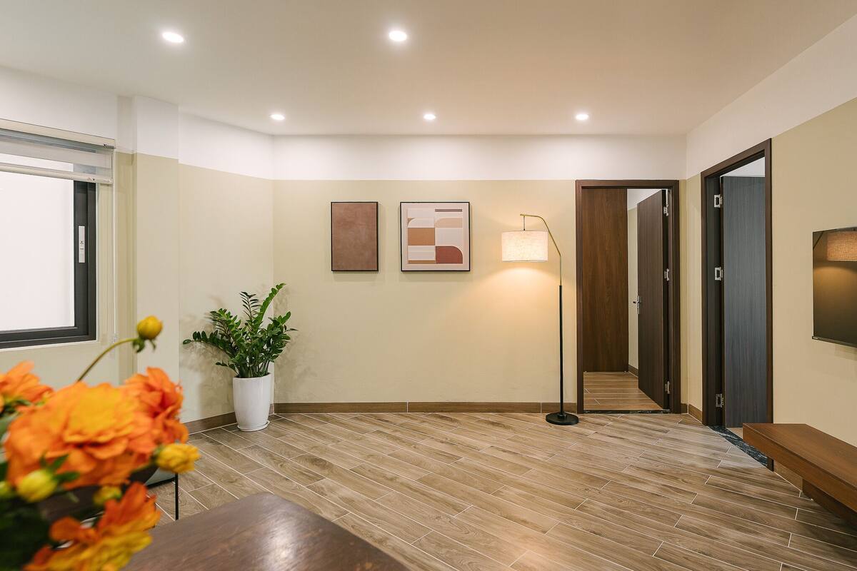 A hallway with wooden flooring, a potted plant, and two framed artworks on the wall.