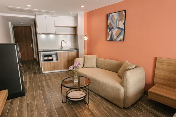 A modern living room with a sofa, a small round table with a vase of flowers, and a kitchen in the background.