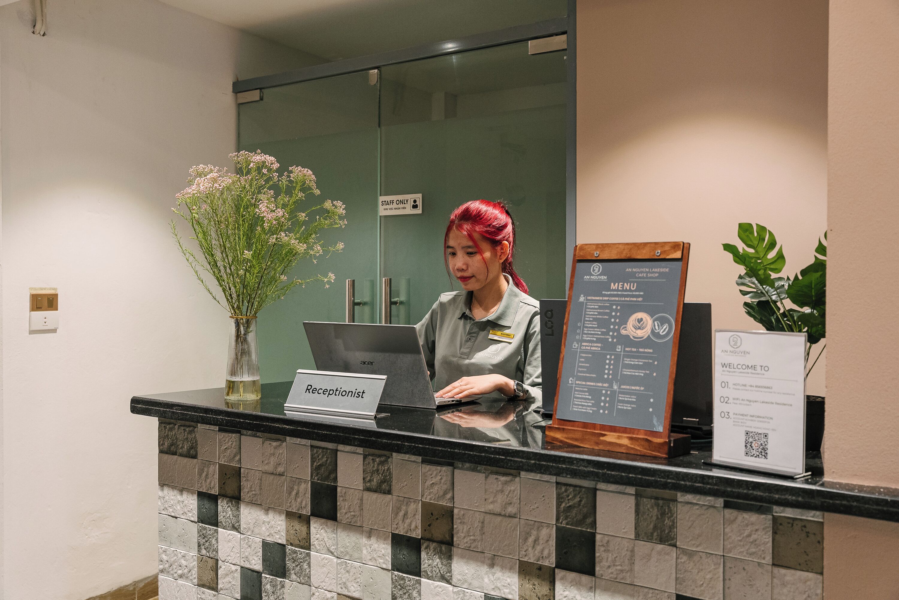 A reception desk with a laptop, a vase of flowers, and a menu sign.