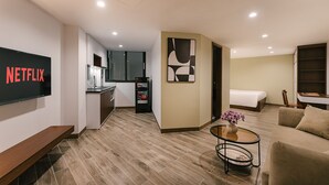 A modern hotel room with a kitchenette, a flat-screen TV, a bed, and a seating area with a small table and a vase of flowers. - An Nguyen Lakeside Residence (Hanoi)