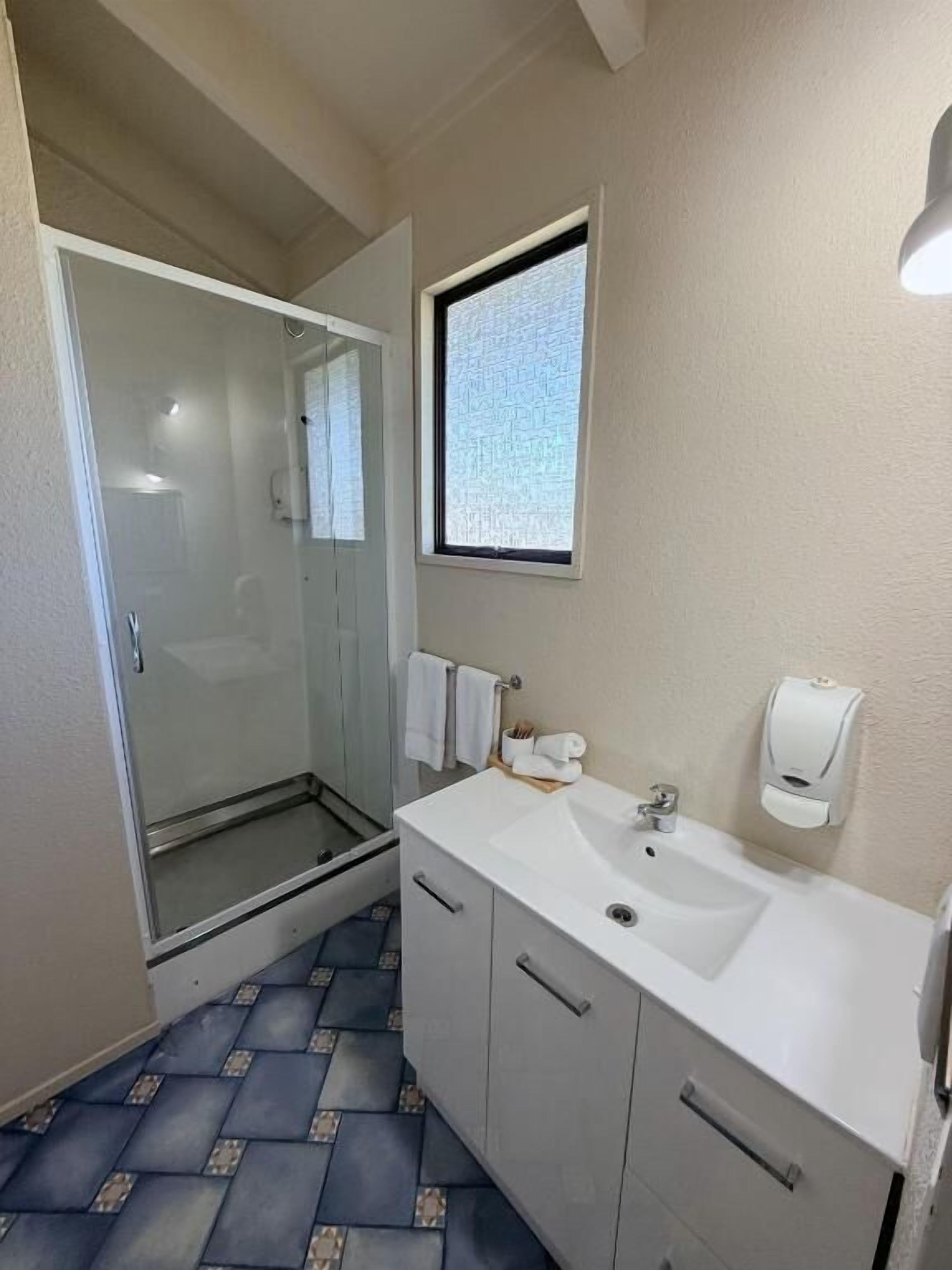 A bathroom with a glass shower enclosure, a white sink, and a window with a view.