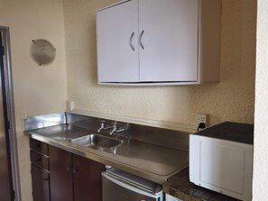 A compact kitchen with a stainless steel countertop, a double sink, and a microwave.