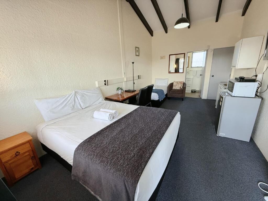 Una habitación de hotel con una cama grande, un escritorio, una silla, un microondas y un mueble pequeño.