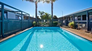 Une piscine à l’eau d’un bleu limpide, entourée d’une clôture et de palmiers.