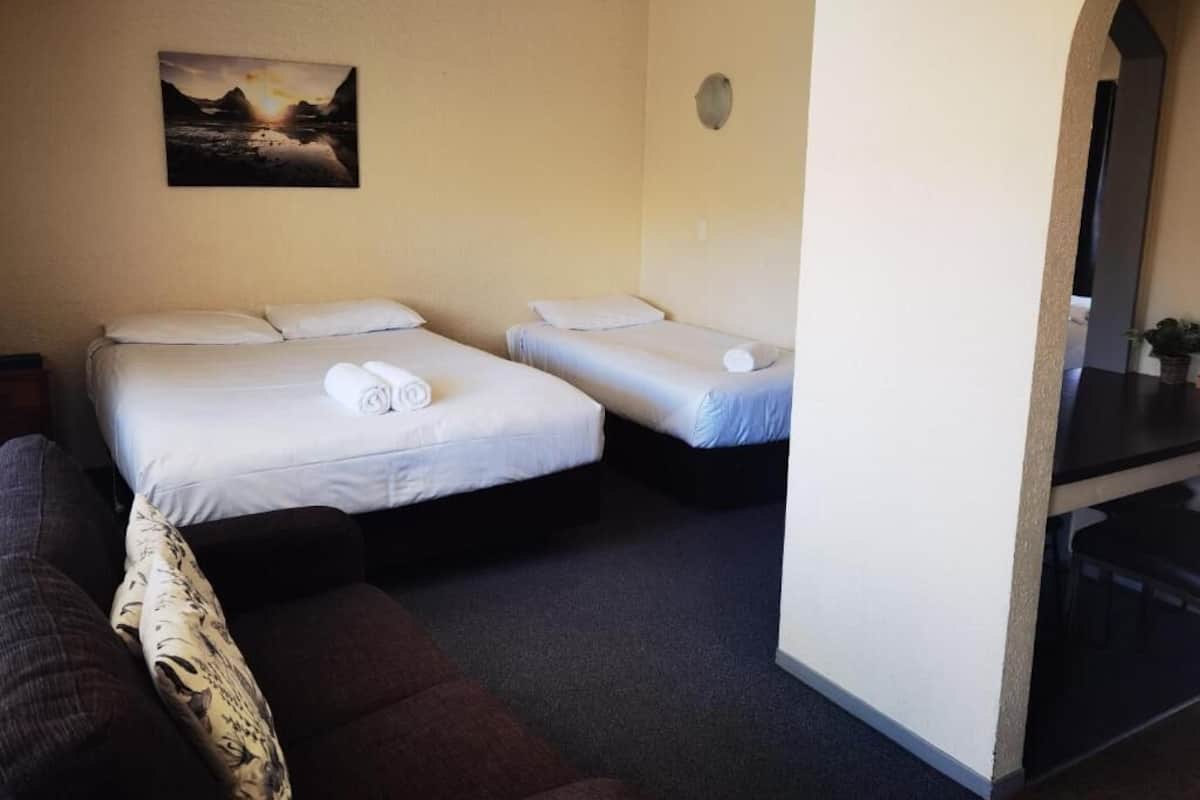 A room with two single beds, a sofa, a painting on the wall, and a small table.